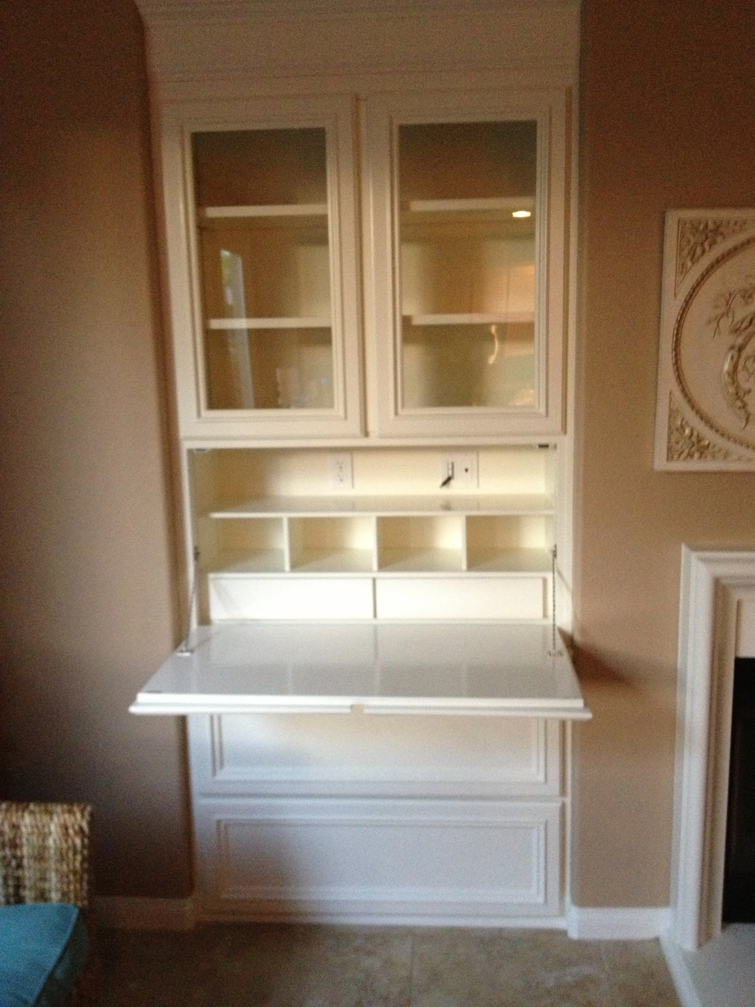 Tall white illuminated secretary cabinet installed between a fireplace and window