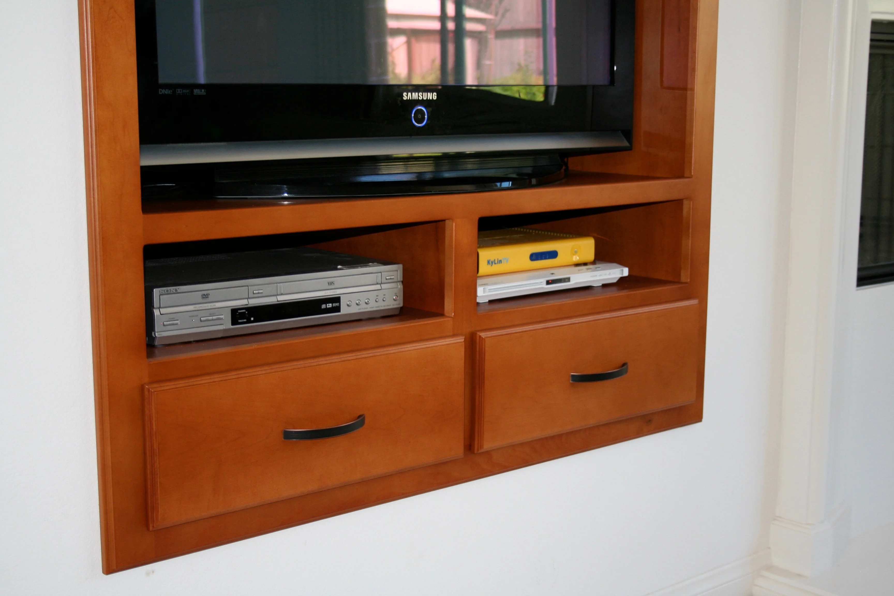 Warm wood media cabinet recessed into a white wall