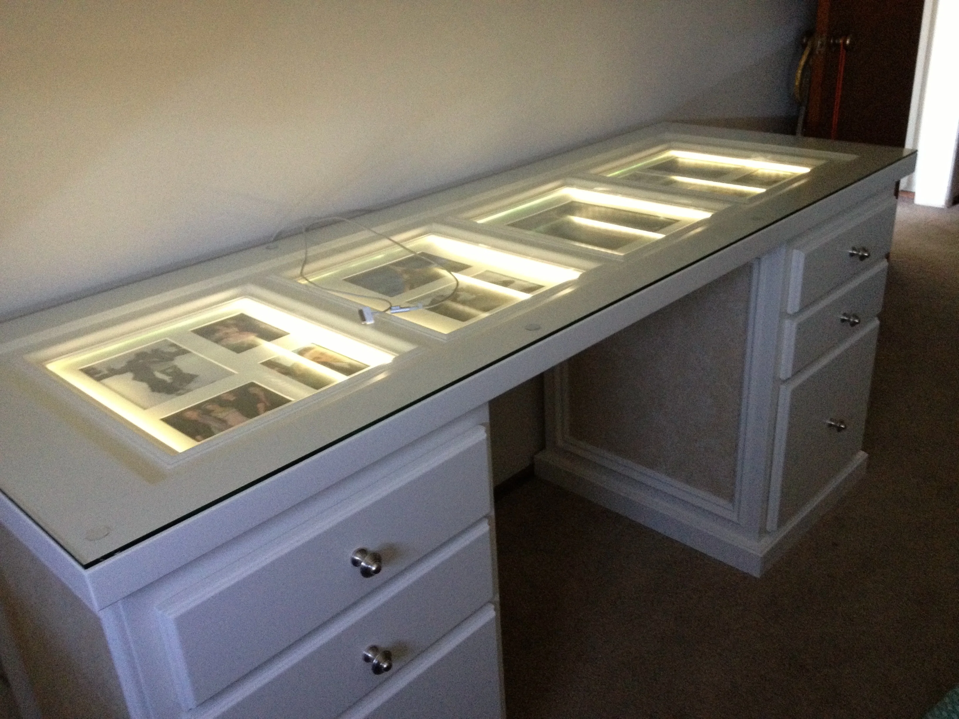 White built-in desk with illuminated photo frames beneath its glass top