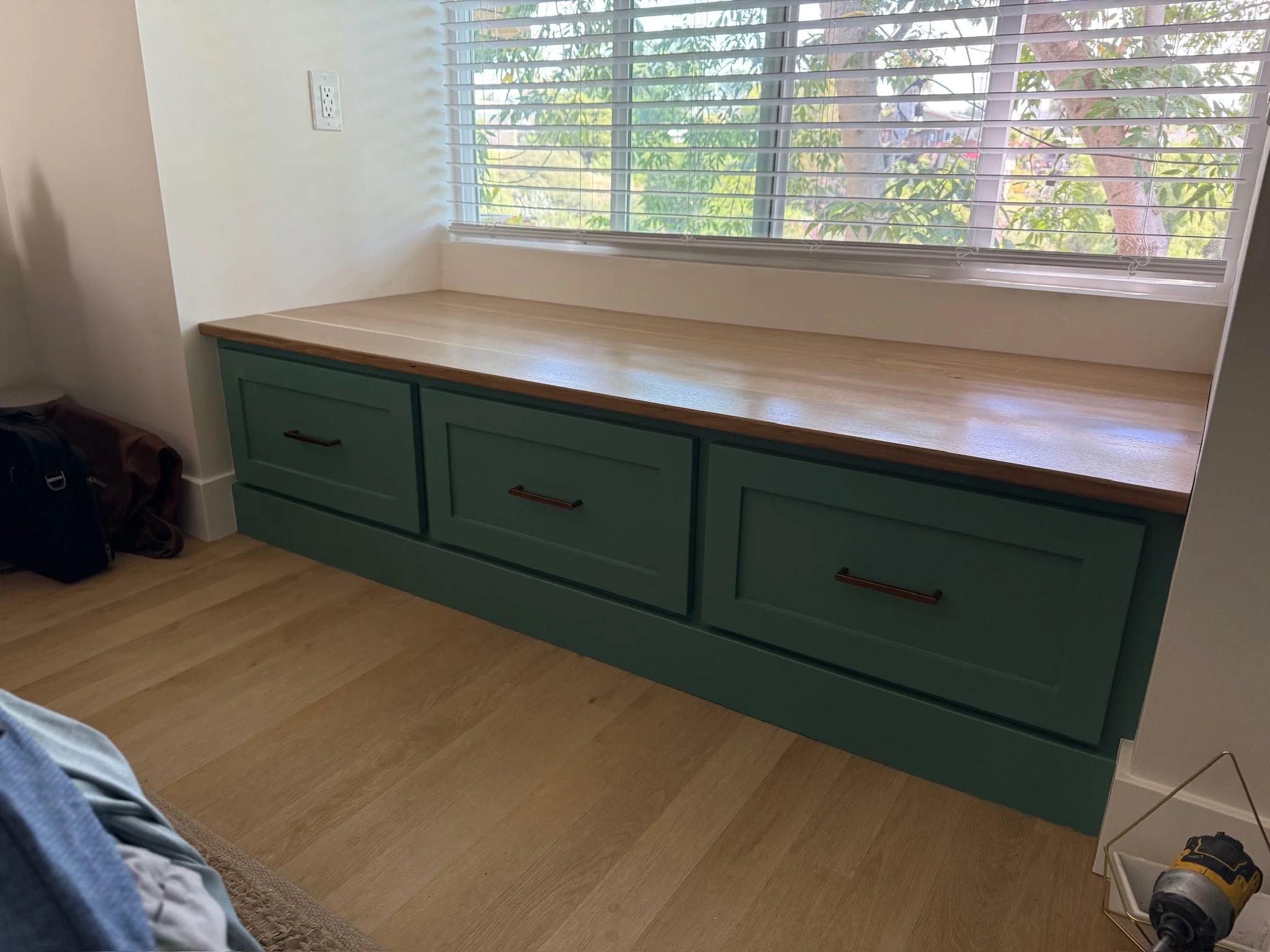 Green built-in window seat with oak top beneath a wide window