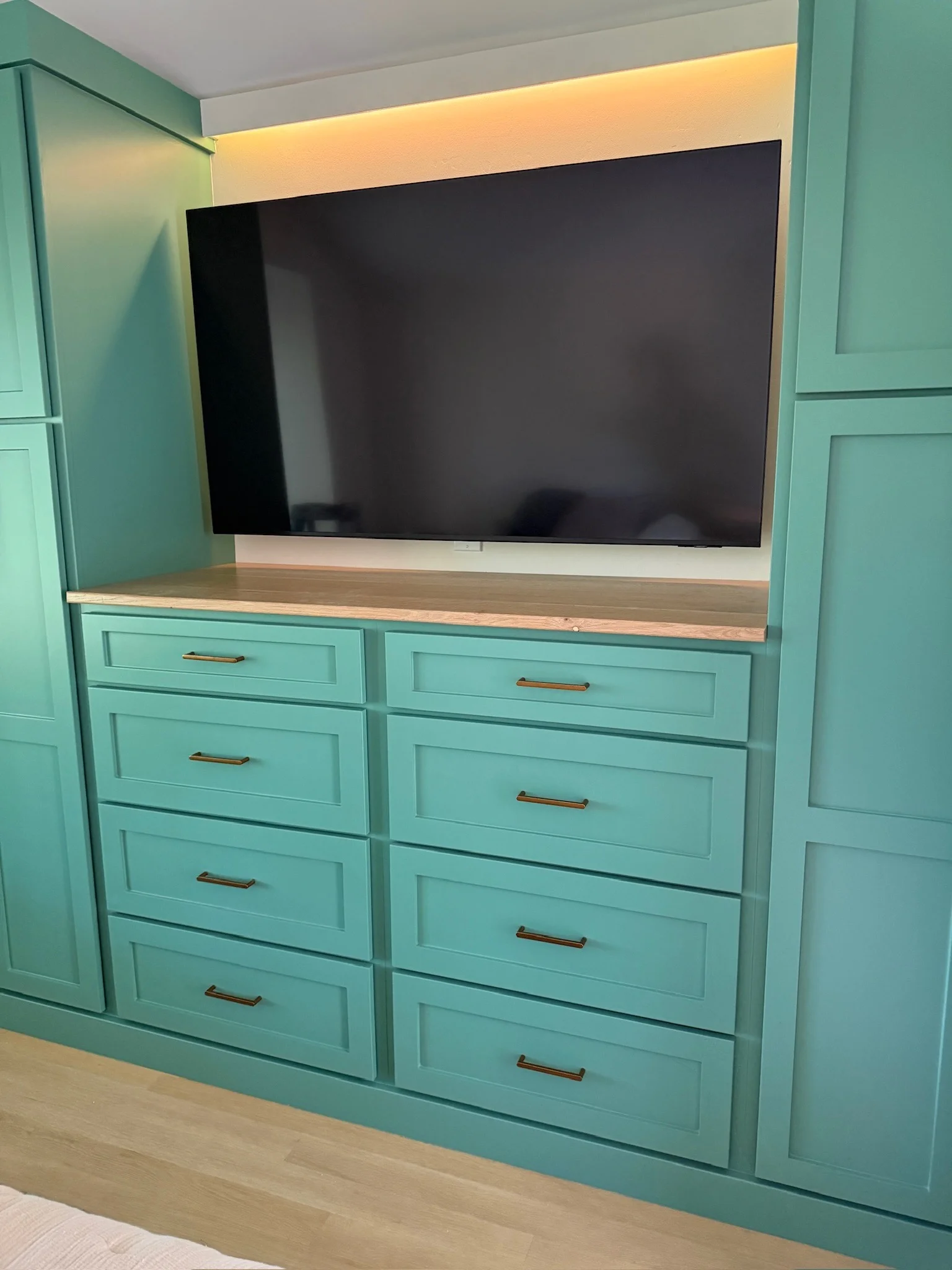 Tall green media built-in with drawers, doors, and oak shelving